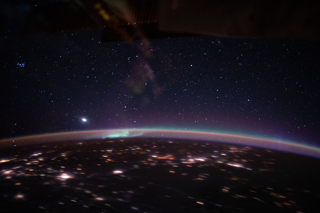 An aurora accents Earth's atmospheric glow underneath a starry sky